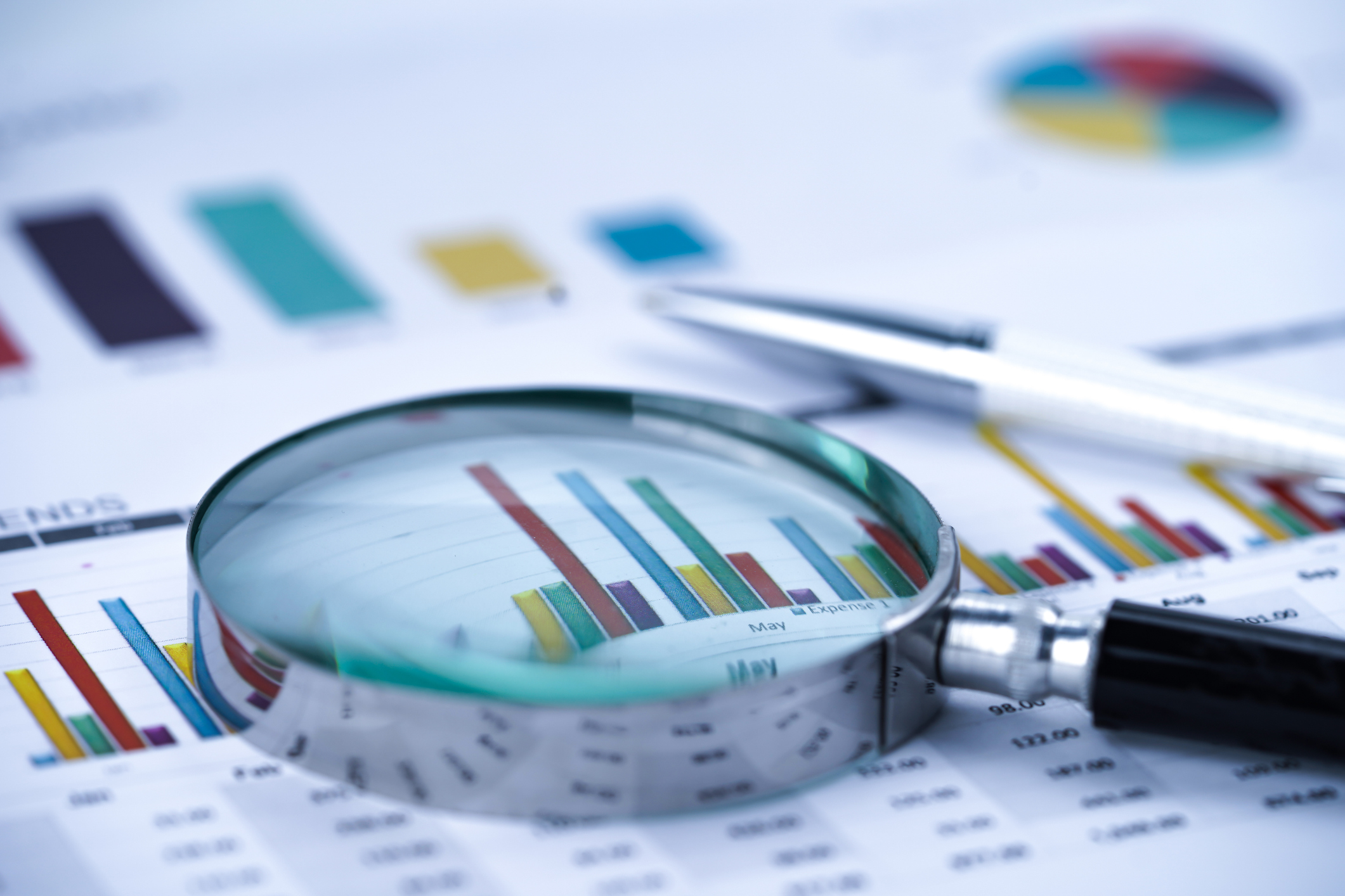 magnifying glass lying on top of a paper report with bar charts and pie graphs