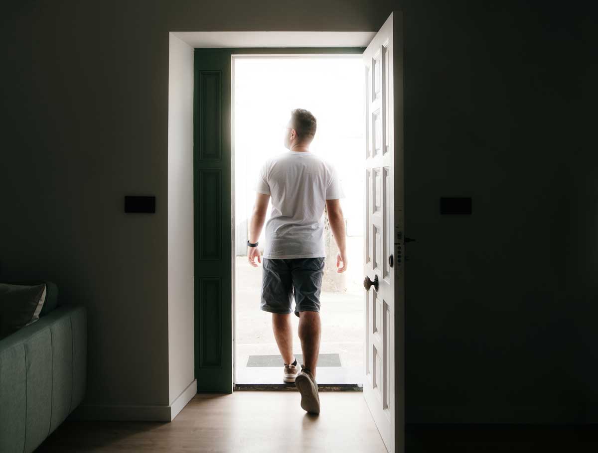 a young man is walking out of a dark room through a door into the light