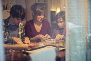 mom and two sons - tween and teen - sit at table decorating cookies