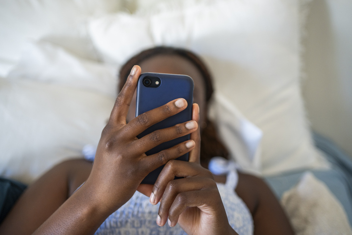 teen girl lying in bed looking at phone