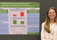 Young woman stands in front of research poster on childhood traum and mental health