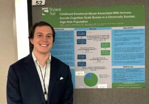 Young man standing in front of research poster on trauma and mental health