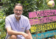 Man kneels next to greenhouse sign