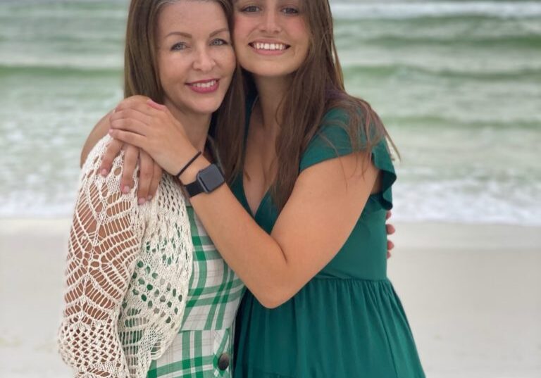 mom with adult daughter hugging on the beach