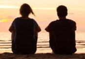 mom and adult son sitting together on beach in silhouette