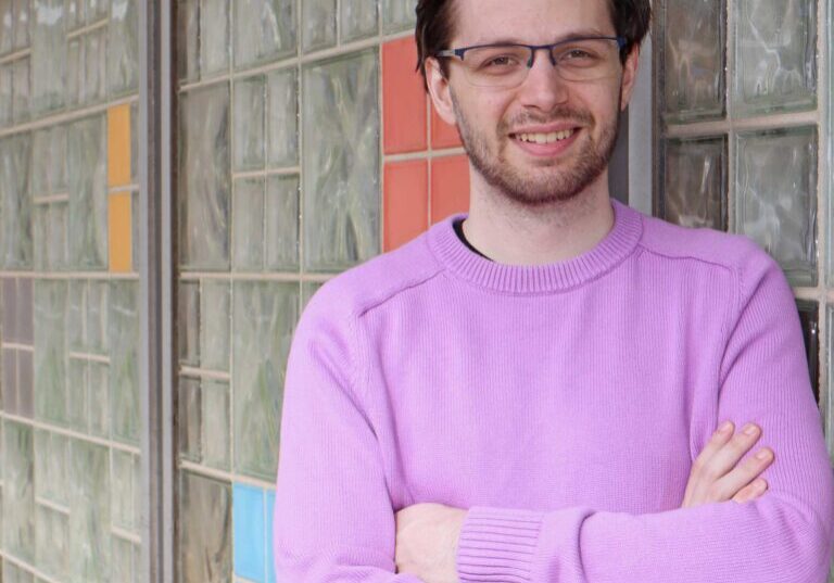 smiling young man in lilac sweater leaning against glass brick wall