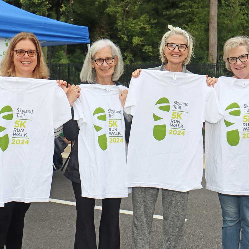 four women hold up 2024 Skyland Trail 5K Run/Walk tshirts and smile