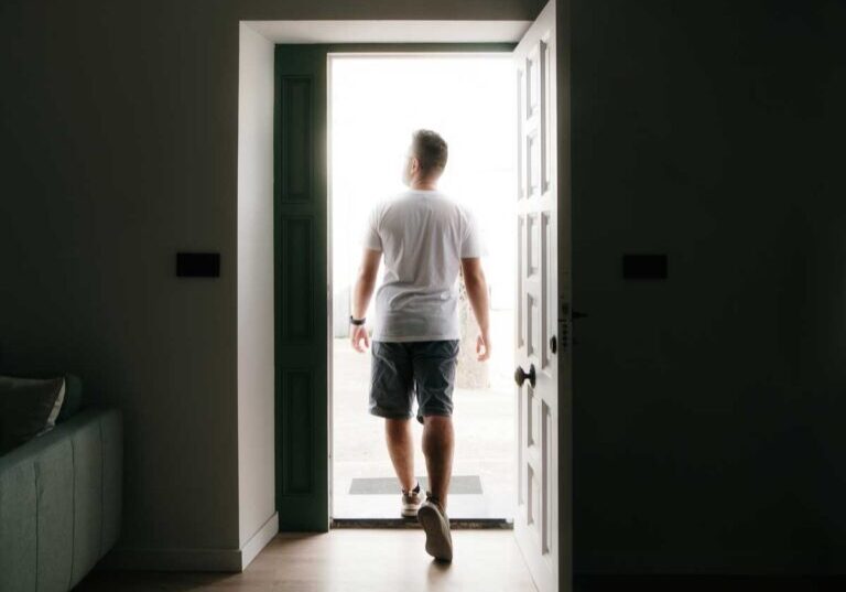 a young man is walking out of a dark room through a door into the light